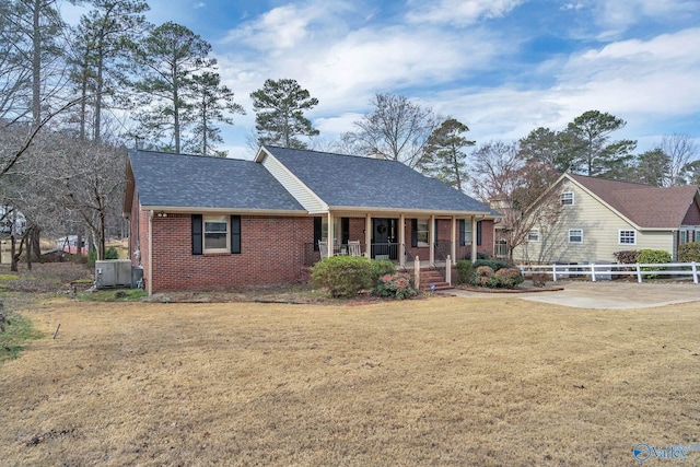 view of front of home with roof with shingles, covered porch, fence, a front lawn, and brick siding