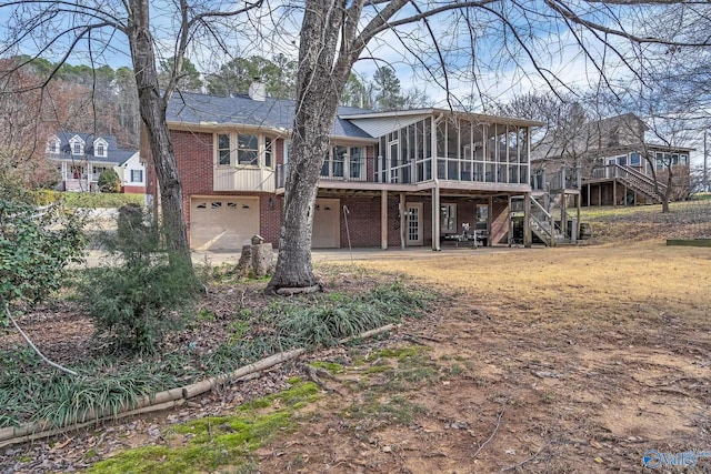 back of property with a sunroom, stairway, an attached garage, a deck, and brick siding