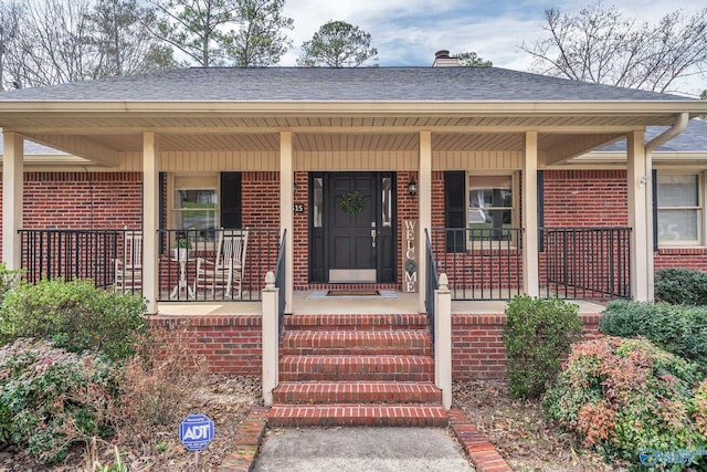 property entrance with a shingled roof, a porch, and brick siding