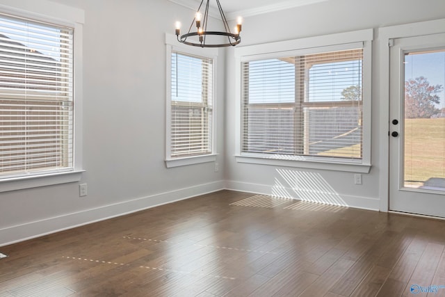 unfurnished dining area with crown molding, a healthy amount of sunlight, dark hardwood / wood-style flooring, and an inviting chandelier