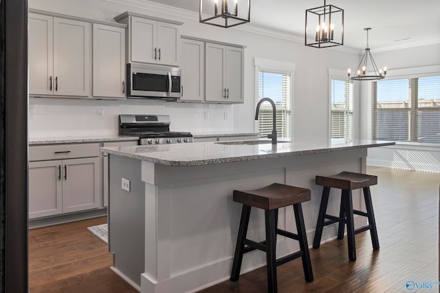 kitchen featuring dark hardwood / wood-style flooring, hanging light fixtures, stainless steel appliances, gray cabinets, and a center island with sink