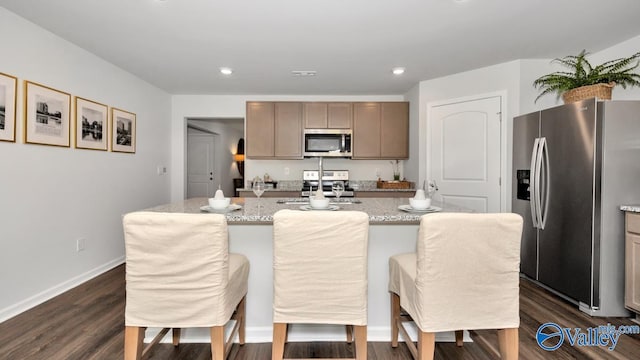 kitchen with light stone counters, a kitchen island with sink, dark hardwood / wood-style flooring, a breakfast bar, and appliances with stainless steel finishes