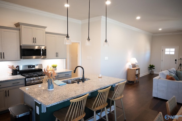 kitchen with appliances with stainless steel finishes, light stone counters, sink, a center island with sink, and hanging light fixtures