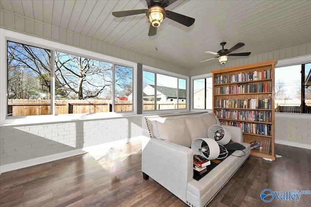 sitting room with ceiling fan, dark hardwood / wood-style floors, and brick wall