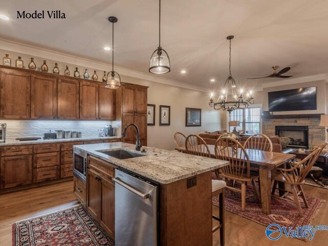 kitchen with light wood-type flooring, a kitchen island with sink, appliances with stainless steel finishes, a fireplace, and ornamental molding