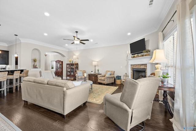 living area featuring arched walkways, a stone fireplace, visible vents, dark wood-style floors, and crown molding