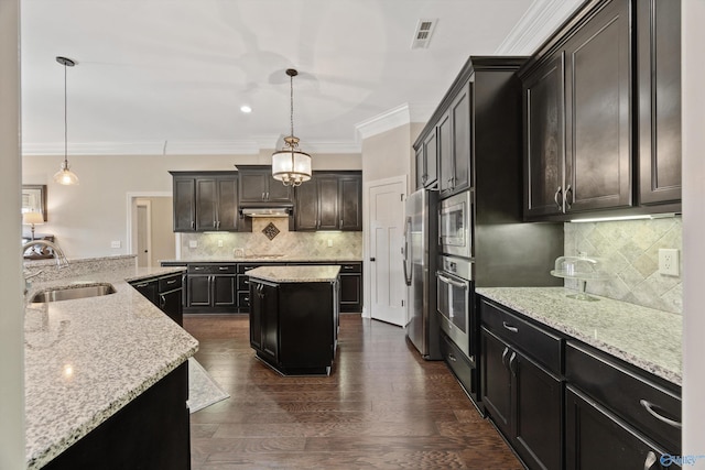 kitchen with a sink, appliances with stainless steel finishes, a kitchen island, and decorative light fixtures