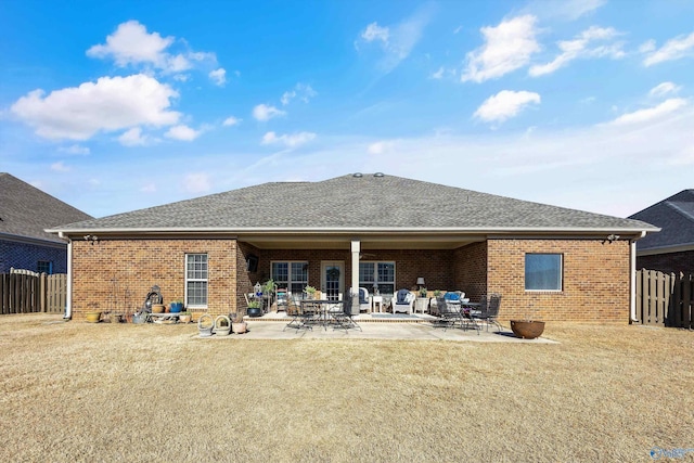 back of property with brick siding, a yard, a shingled roof, a patio area, and fence