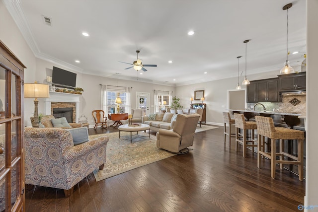 living area featuring a stone fireplace, dark wood finished floors, visible vents, and crown molding