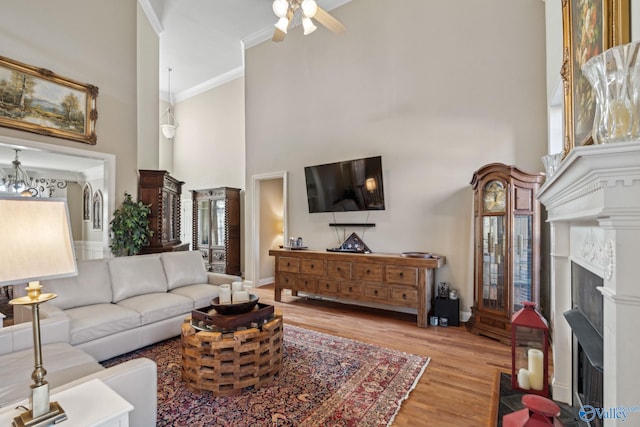 living room with crown molding, plenty of natural light, a towering ceiling, and light hardwood / wood-style floors