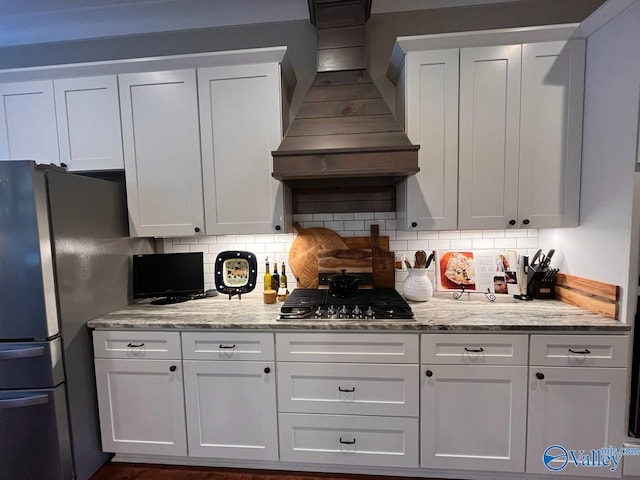 kitchen featuring white cabinetry, light stone counters, tasteful backsplash, custom exhaust hood, and appliances with stainless steel finishes