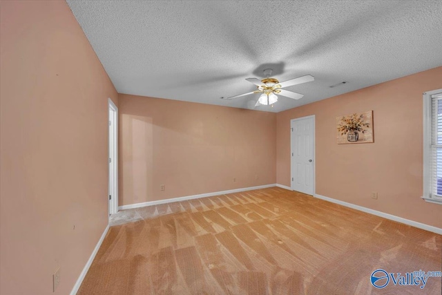 spare room featuring visible vents, baseboards, light colored carpet, ceiling fan, and a textured ceiling