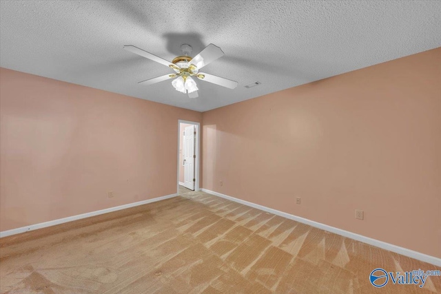 spare room with light colored carpet, ceiling fan, a textured ceiling, and baseboards