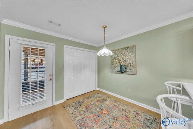 interior space featuring crown molding, visible vents, a textured ceiling, wood finished floors, and baseboards