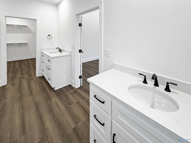 full bathroom featuring a spacious closet, wood finished floors, two vanities, and a sink