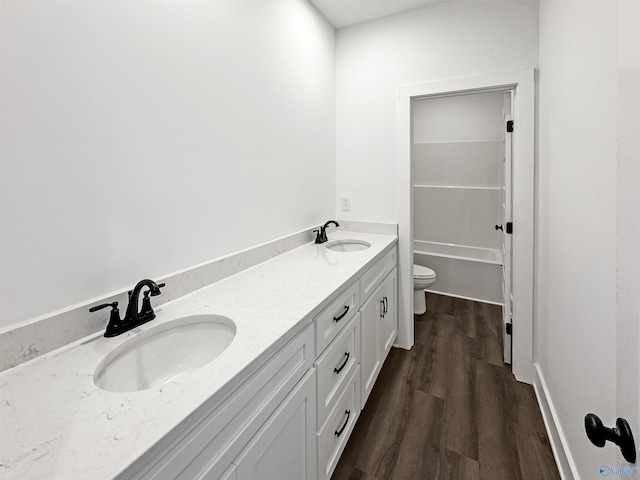 bathroom with double vanity, wood finished floors, a sink, and toilet