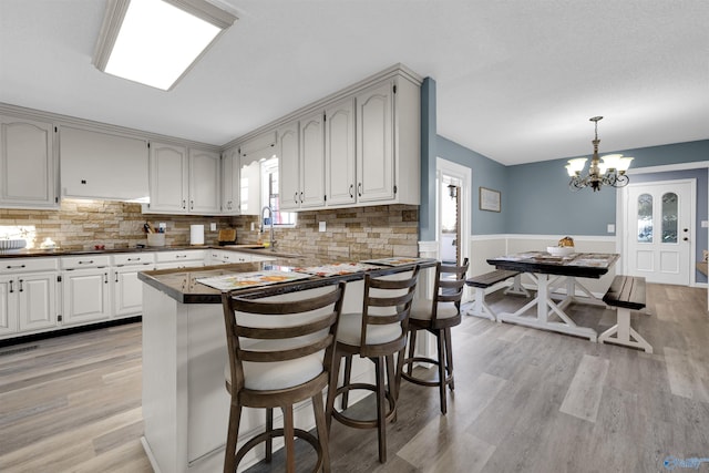 kitchen featuring a notable chandelier, light hardwood / wood-style floors, decorative light fixtures, decorative backsplash, and a breakfast bar