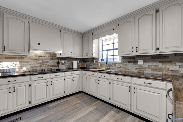 kitchen with black electric stovetop, backsplash, sink, light hardwood / wood-style flooring, and white cabinets