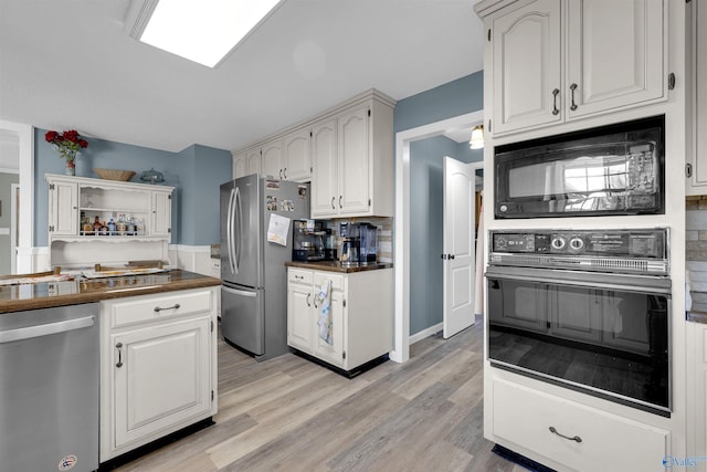 kitchen with light wood-type flooring, backsplash, black appliances, white cabinets, and butcher block counters