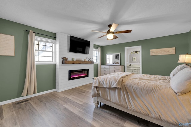 bedroom featuring a fireplace, a textured ceiling, light hardwood / wood-style flooring, and ceiling fan