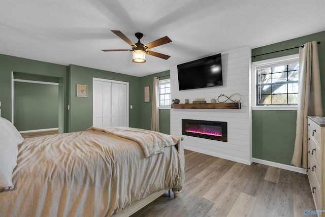 bedroom with ceiling fan, a large fireplace, light hardwood / wood-style flooring, a textured ceiling, and a closet