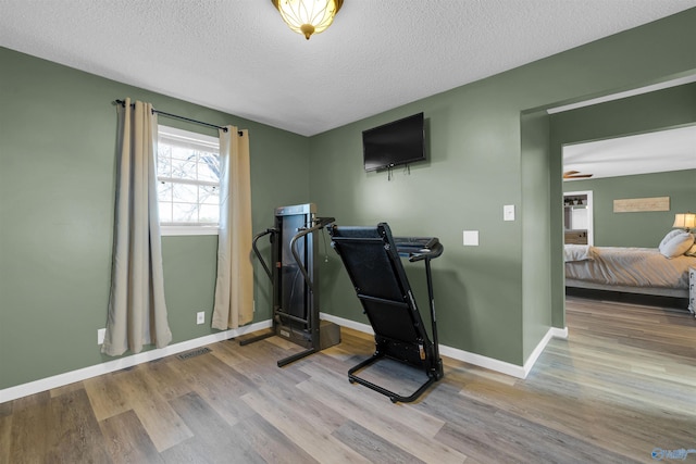 workout room with light wood-type flooring, a textured ceiling, and ceiling fan