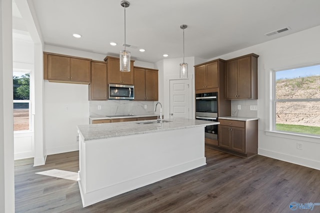 kitchen with sink, tasteful backsplash, light stone counters, a center island with sink, and appliances with stainless steel finishes