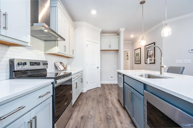 kitchen with pendant lighting, white cabinetry, sink, stainless steel appliances, and wall chimney range hood