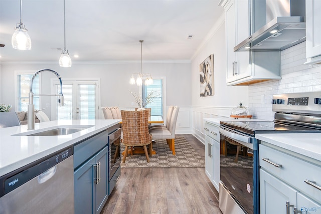 kitchen with sink, appliances with stainless steel finishes, white cabinetry, hanging light fixtures, and wall chimney exhaust hood