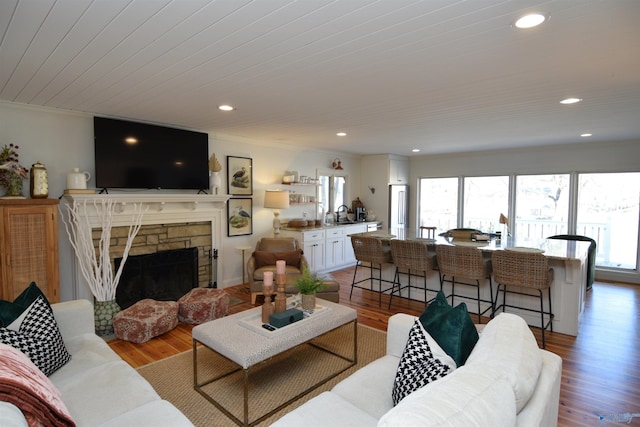 living room featuring sink, wood ceiling, a fireplace, ornamental molding, and light wood-type flooring