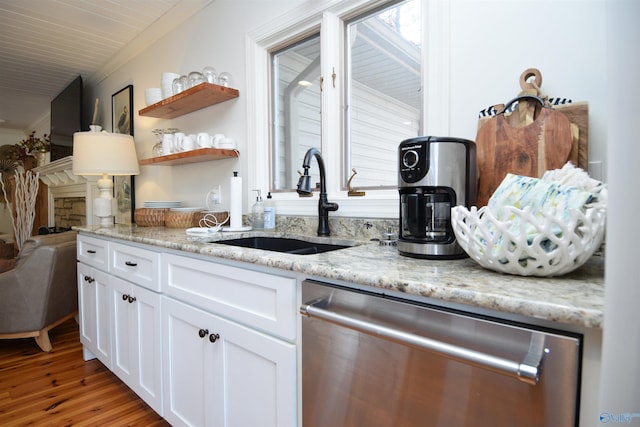 kitchen featuring sink, white cabinetry, light stone counters, wood-type flooring, and stainless steel dishwasher