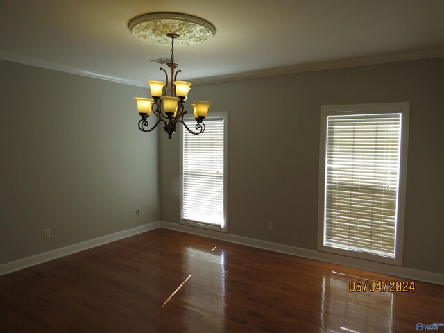 spare room with crown molding, dark wood-type flooring, and a notable chandelier