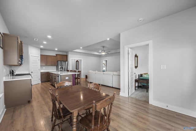 dining space with a ceiling fan, a tray ceiling, wood finished floors, and recessed lighting