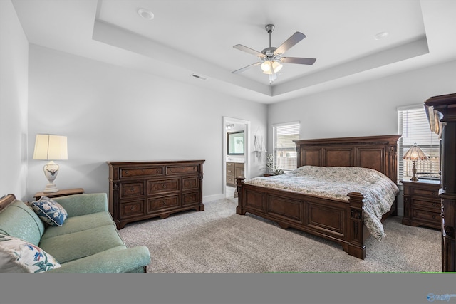 bedroom featuring ensuite bathroom, a tray ceiling, visible vents, and light colored carpet