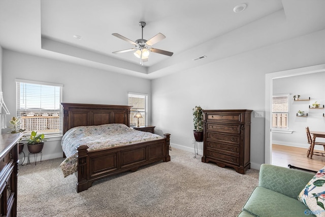 bedroom featuring a tray ceiling, a ceiling fan, visible vents, and baseboards