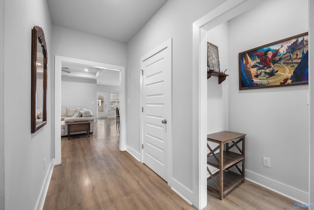 corridor featuring light wood-style floors, baseboards, and a tray ceiling