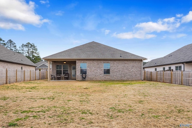 rear view of house featuring a fenced backyard, a shingled roof, a lawn, and brick siding