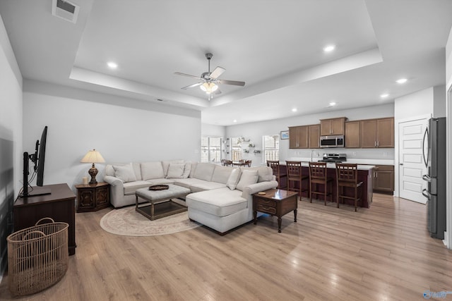 living area with light wood-type flooring, visible vents, a raised ceiling, and recessed lighting