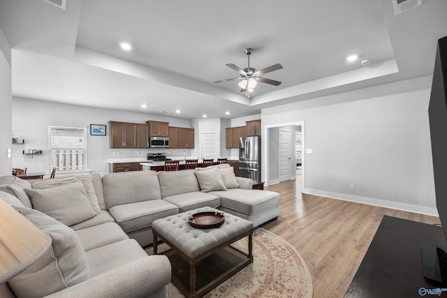 living room with a raised ceiling, visible vents, light wood-style floors, ceiling fan, and baseboards