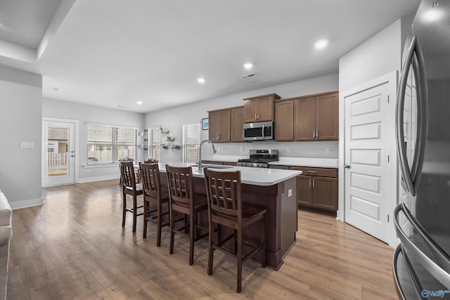 kitchen featuring appliances with stainless steel finishes, light wood-style floors, a sink, an island with sink, and a kitchen bar