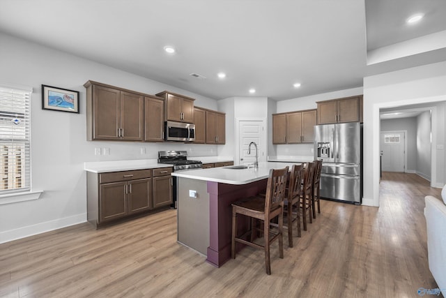 kitchen featuring light wood finished floors, stainless steel appliances, visible vents, a sink, and a kitchen breakfast bar