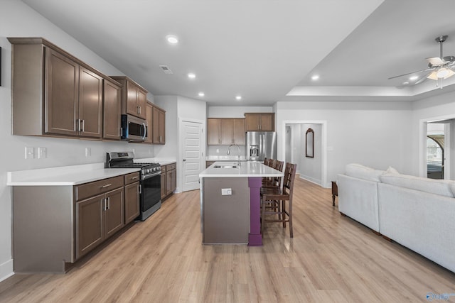 kitchen featuring open floor plan, appliances with stainless steel finishes, light wood finished floors, and a kitchen breakfast bar