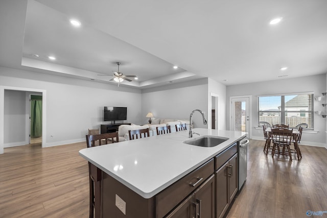 kitchen with a raised ceiling, dishwasher, wood finished floors, light countertops, and a sink