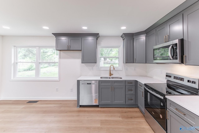 kitchen with a sink, gray cabinetry, stainless steel appliances, light countertops, and light wood-type flooring