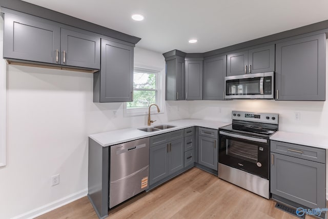 kitchen featuring stainless steel appliances, light countertops, light wood-style flooring, and a sink