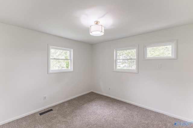 carpeted empty room with a wealth of natural light, visible vents, and baseboards