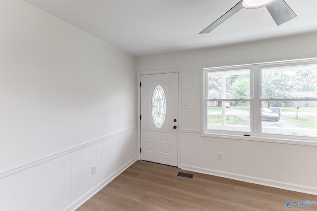 entryway with visible vents, ornamental molding, light wood-type flooring, and wainscoting