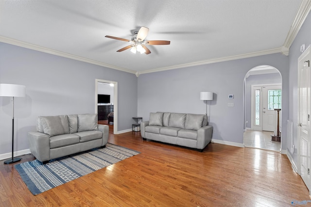 living area featuring ornamental molding, arched walkways, a ceiling fan, and wood finished floors