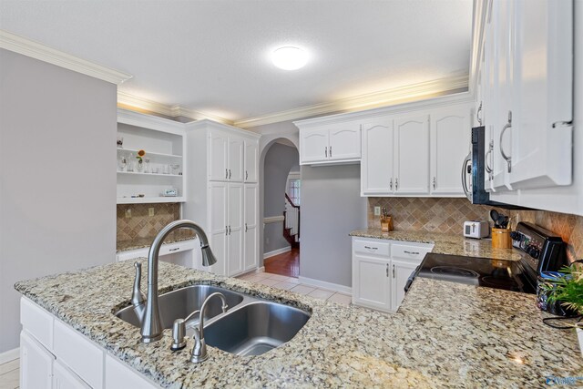 kitchen with a sink, range with electric cooktop, tasteful backsplash, baseboards, and arched walkways