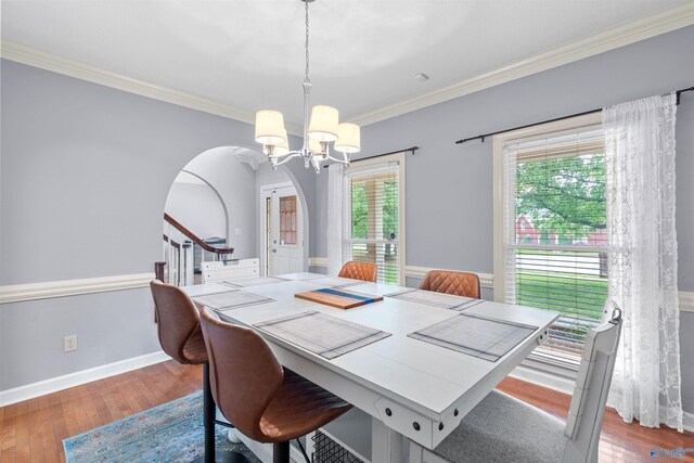 dining area with crown molding, arched walkways, an inviting chandelier, and wood finished floors